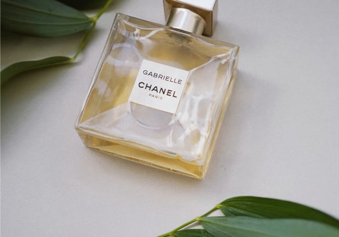 Chanel Perfume, Gabrielle next to some green leafs, on a white background